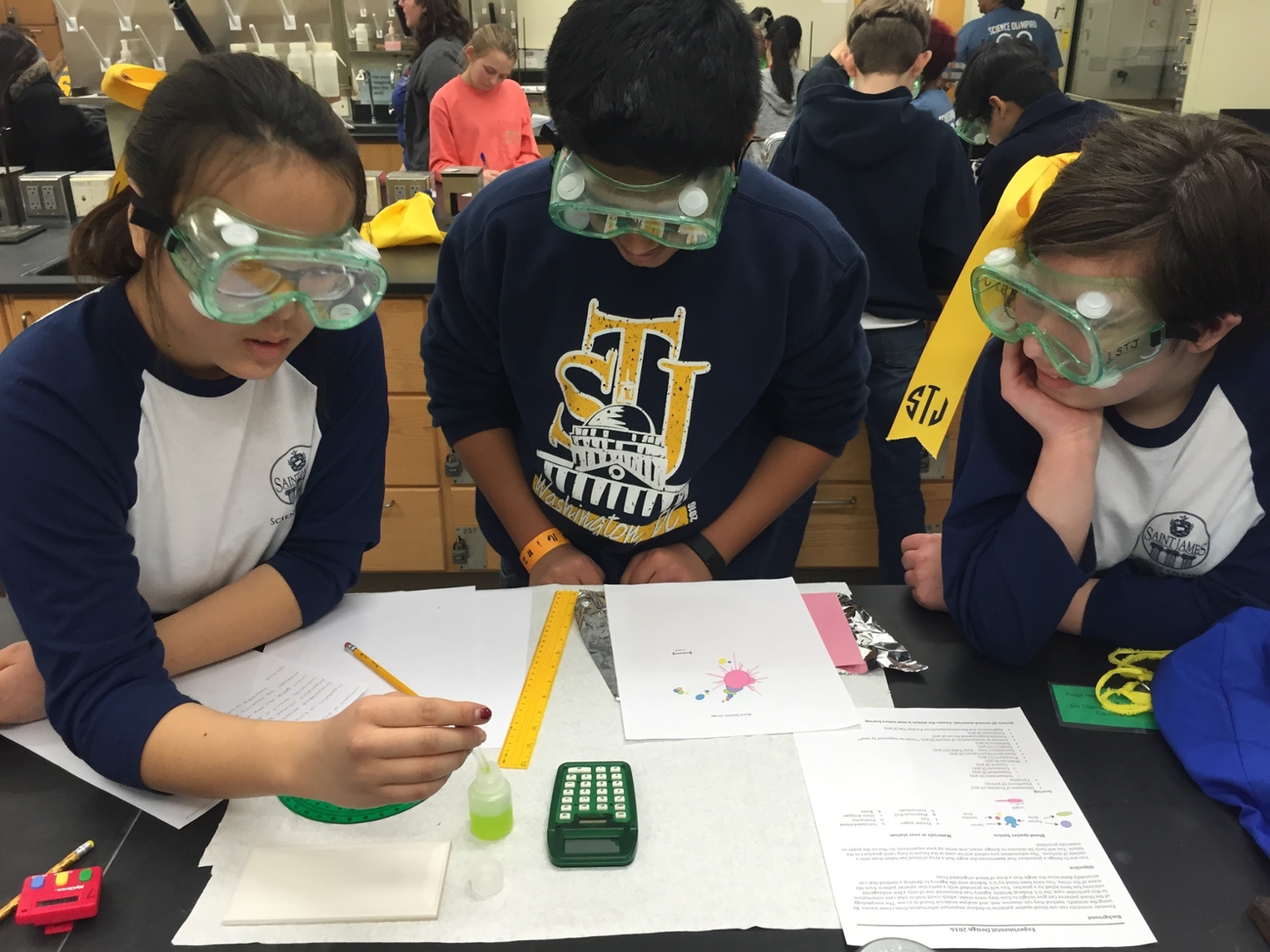 three science olympiad students with googles working at a lab table