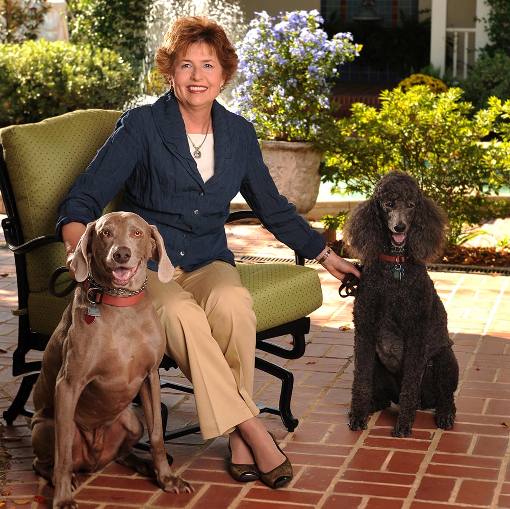 Susie Gogue sits on a bench as her two dogs , Pogo and Sophie, sit next to her.