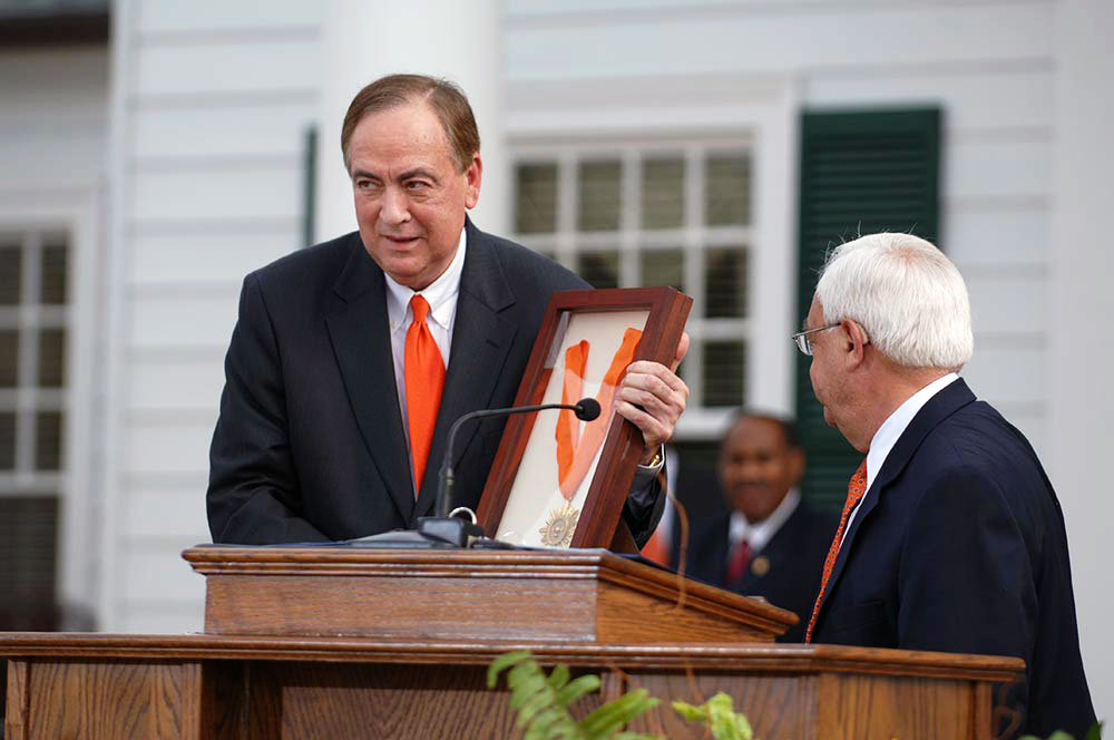 Paul Spina stands at the podium at President Jay Gogue holds up a framed medal.