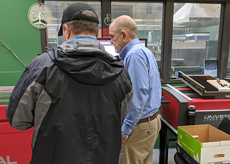 Two men standing in front of laser cutting machine.