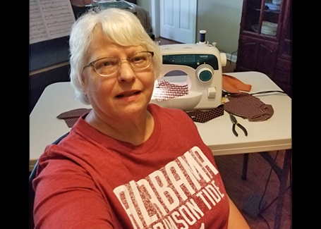 Woman sits in front of sewing machine wearing maroon Alabama Crimson tide shirt.