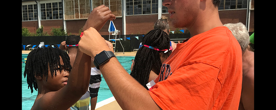 Young boy holds up his arm to get armband put on for passing his swimming test