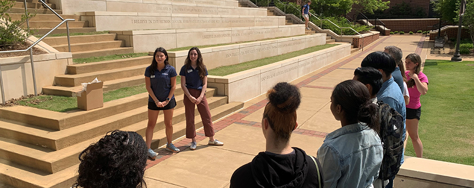 2 female campus tour guides begin a tour with a small group of male and female students 