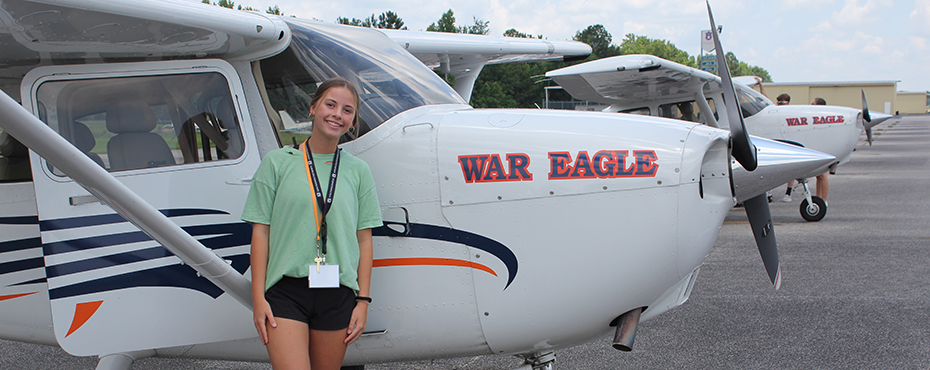 Young female camper poses for photo in front of AU plane with 'War Eagle' printed on the nose of plane