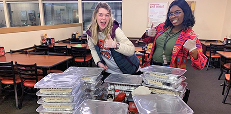 Two girls give thumbs up in front of pans of donated food