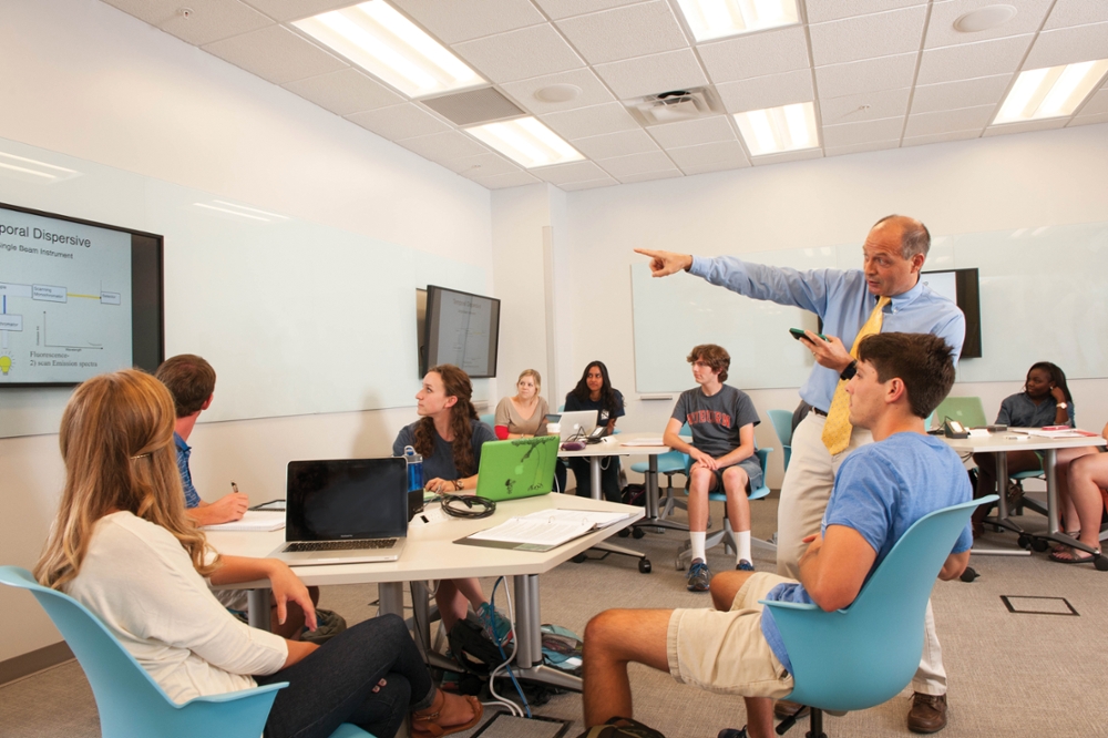 Professor Vince Ortiz engages with students who sit around hexagonal tables in the EASL classroom