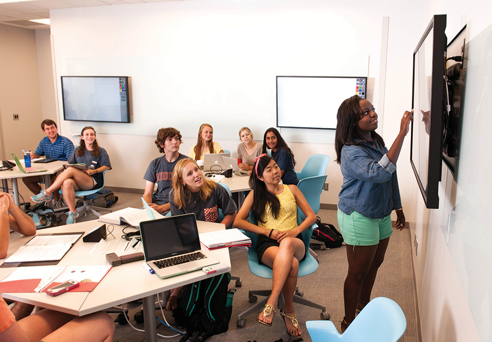 A student writes on a digital display in the EASL room while other students look on
