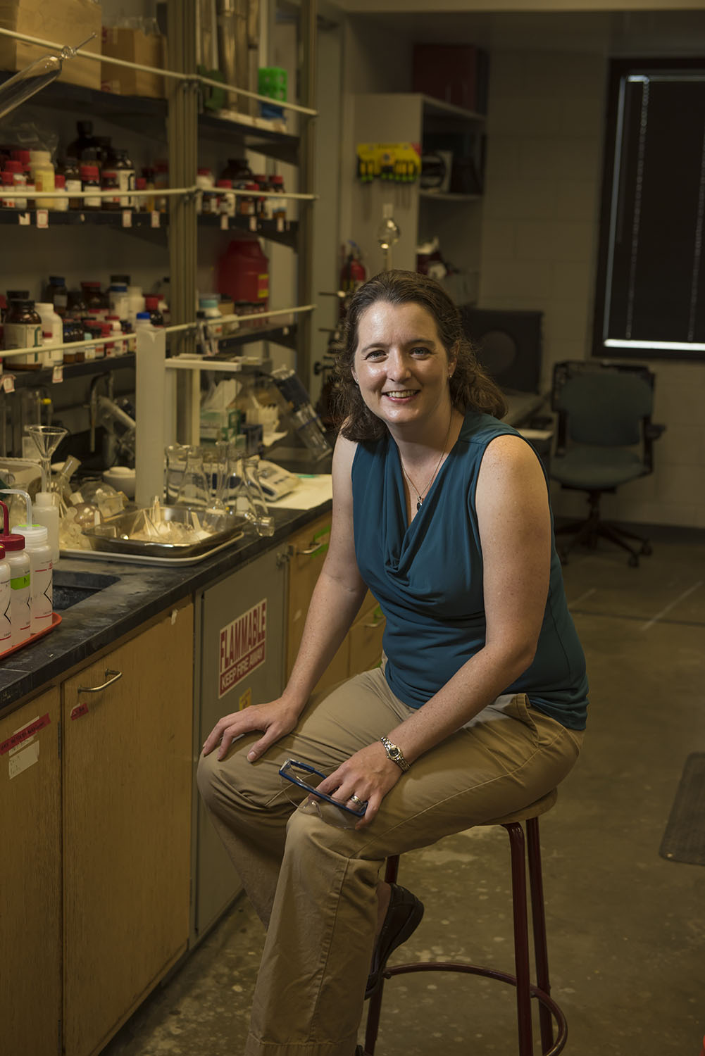 Anne Gorden sitting on a stool in her lab with equipment on the bench in the background