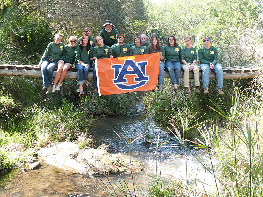 Group photo of Dr. Best and students on a wooden bridge in Swaziland holding an Auburn Flag