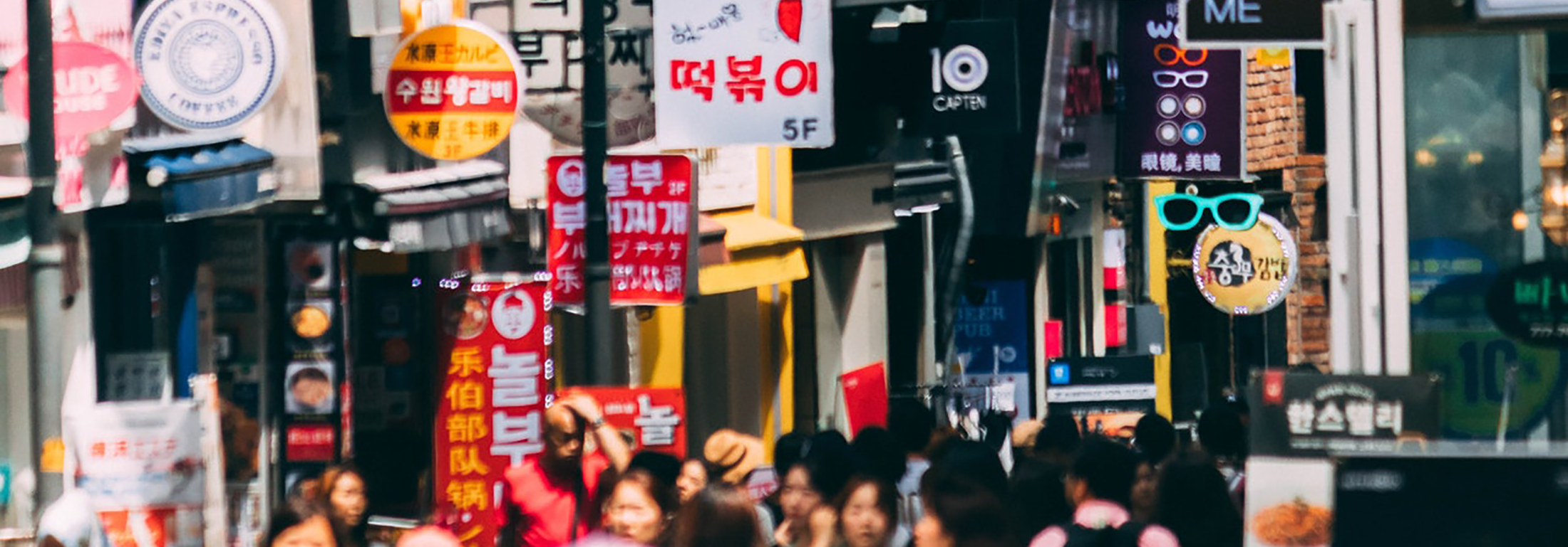 Street scene with many signs in different languages and people on the sidewalk