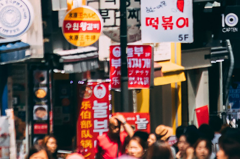 Street scene with many signs in different languages and people on the sidewalks