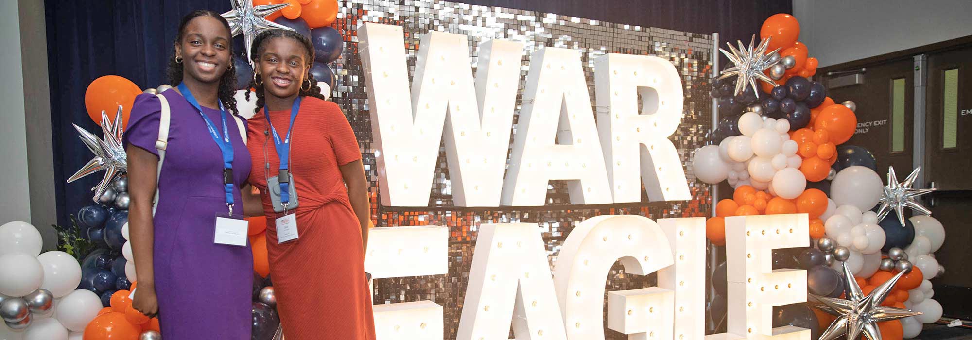 Two students in front of a War Eagle sign