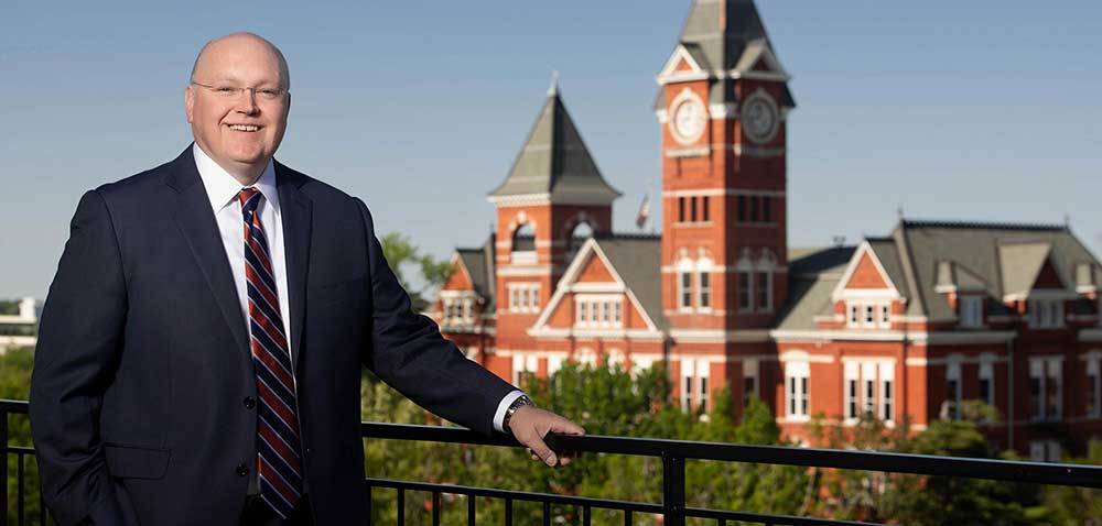 Christopher Roberts on a balcony with Samford Hall in the background.