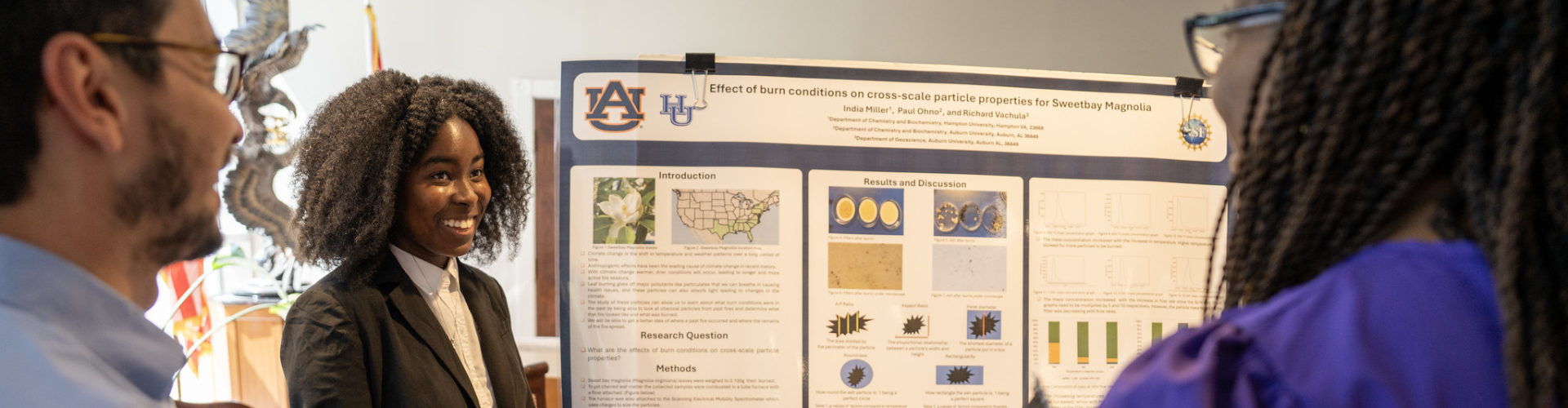 A student presenter stands beside a research poster and smiles while speaking with two attendees during a poster presentation event.