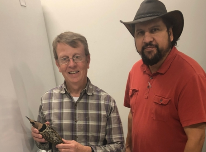 Geoff Hill, holding a bird specimen, and standing with David Laurencio