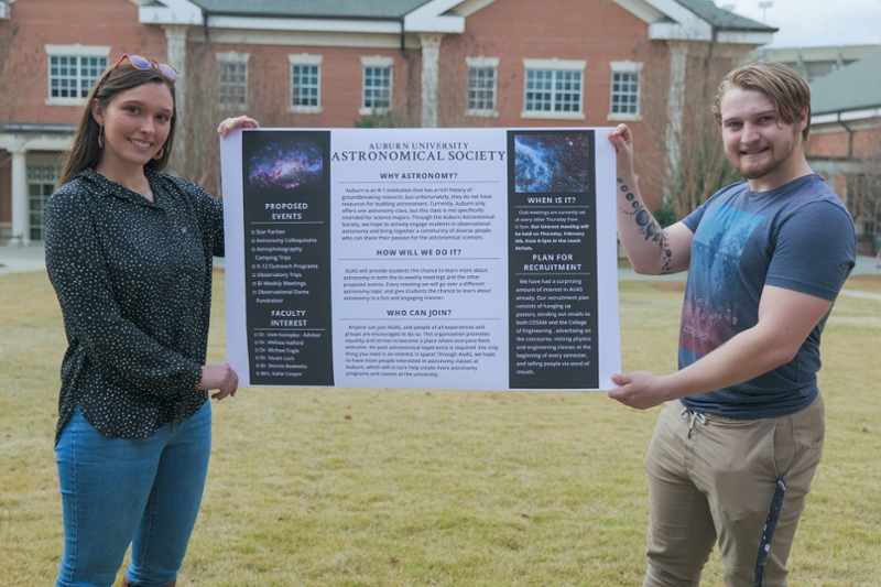Students holding a poster to promote the Auburn Astronomical Society. 