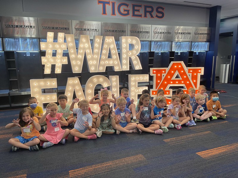 Students in the Office of Outreach's Camps sitting in front of a War Eagle sign