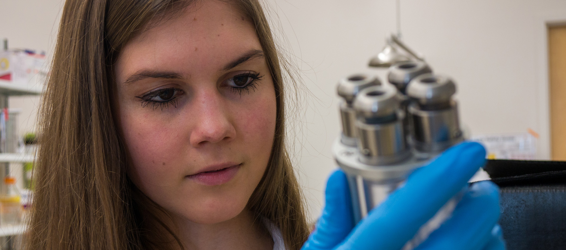 female student in lab holding small piece of equipment