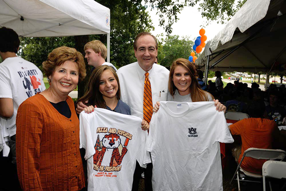 President Jay Gogue and his wife, Susie, stand with two students who are holding up T-shirts featuring the logo for Pizza and Popsicles with the President.