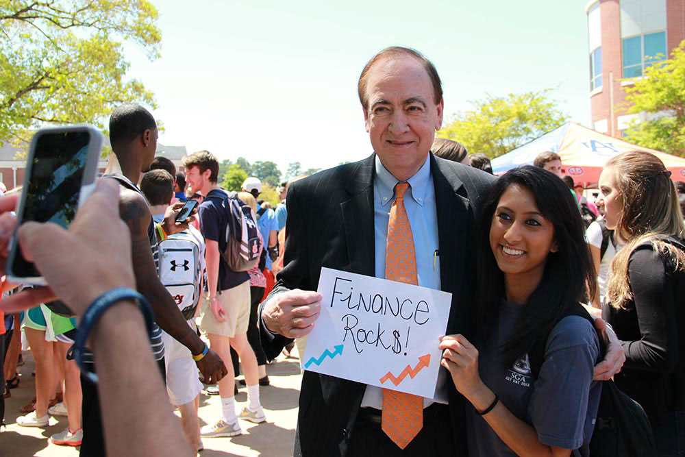 Jay Gogue and a student pose for a picture. The president and student are holding a sign that says 'Finance Rocks!'