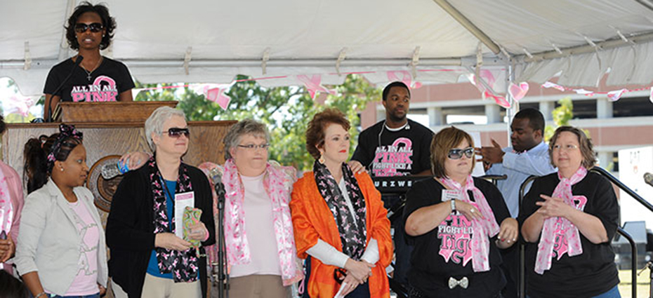 Group of breast cancer survivors wearing decorative scarfs stand in front of audience to be recognized