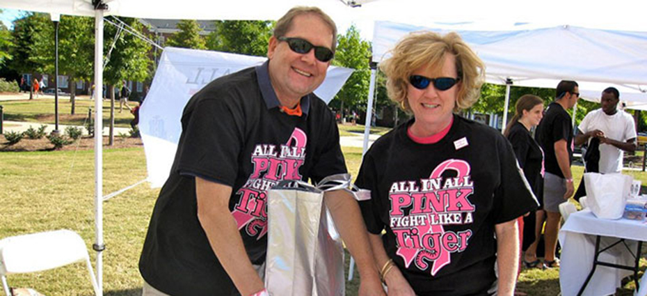 A man and woman wearing black all in all pink shirts set up items on their display table