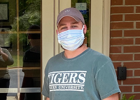 Aaron Carpenter stands in front of building with medical face mask on.