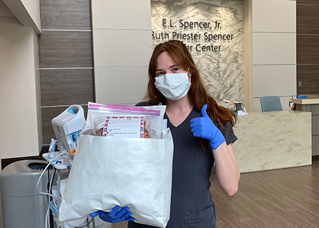 Female wearing scrubs and mask holds up envelope full of masks at EAMC Cancer Center.