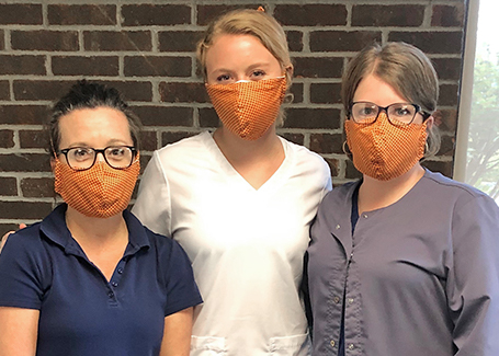 Three girls pose for photo wearing orange and blue face masks.