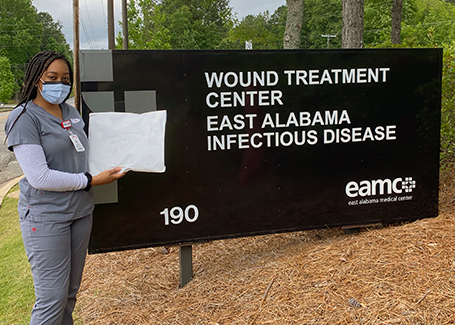 Woman in scrubs stands next to large stone sign that reads Wound Treatment Center East Alabama Infectious Disease