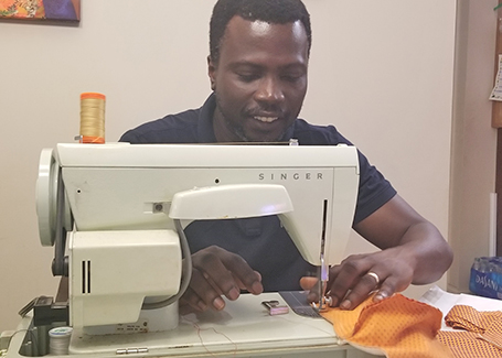 Joseph Emmanuel Quansah sitting at sewing machine making masks