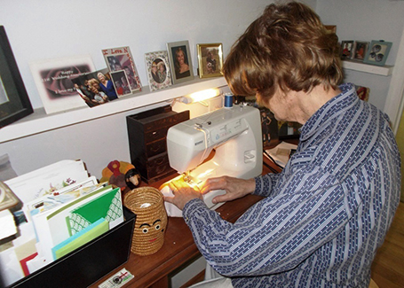 Sue Mason sitting at sewing machine making masks