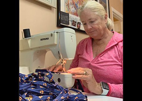 Woman uses sewing machine to sew blue and orange mask ties.