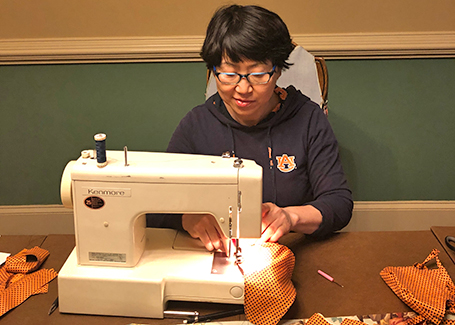 Dong Shang sits behind sewing machine making a fabric face mask.