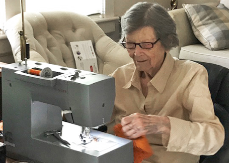 Woman sits at sewing machine making orange and blue face masks