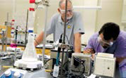 Two men wearing lab googles examine science instruments