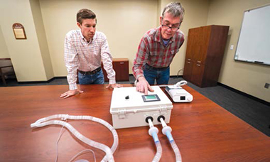 Two men standing in front of table looking at CPAP machine