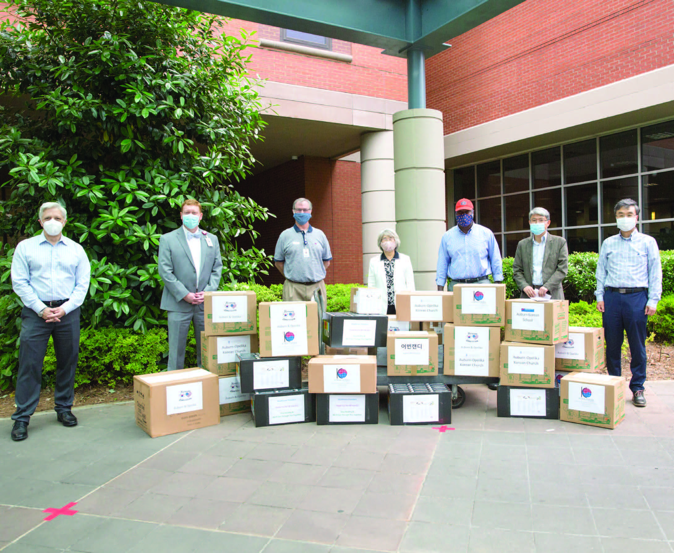 People wearing face masks pose behind boxes of donation materials in front of hospital