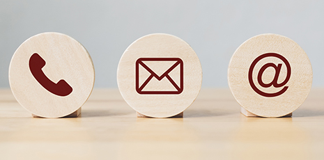 Three icons, email, phone, and at symbol sitting on wood background