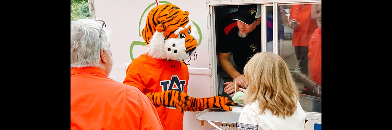 Aubie the Tiger stands at window of O Town ice cream truck while speaking with passerbys