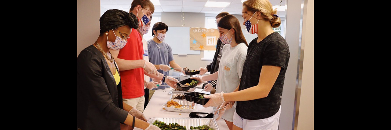 Campus kitchens volunteers stand on either side of table while packaging food