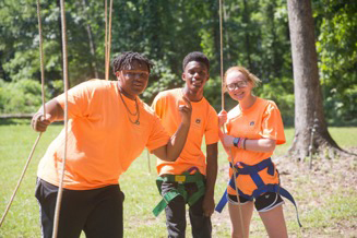 Three young adults give a thumbs up to the camera during the ropes course as part of leadership and teambuilding.
