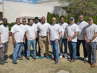 Group of men wearing grey shirts pose for group photo outside