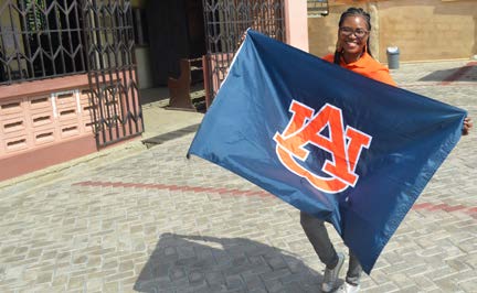Mac-Jane smiling holding navy blue flag with orange AU interlocking logo on it.