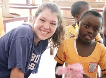 Hannah poses for photo with young Ghanian girl wearing yellow shirt.