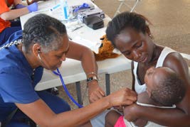Woman in scrubs uses stethoscope to listen to child's heart at clinic in Ghana
