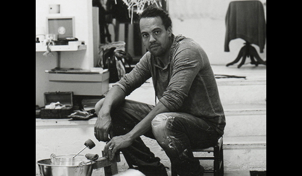 Black and white photo of man squatting down near art supplies