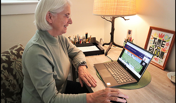 Older woman smiles while looking at OLLI website on laptop screen