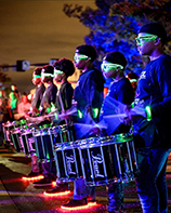 A line of young people wearing neon colored glasses and holding drums