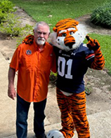 Man with white hair and beard standing next to a tiger mascot